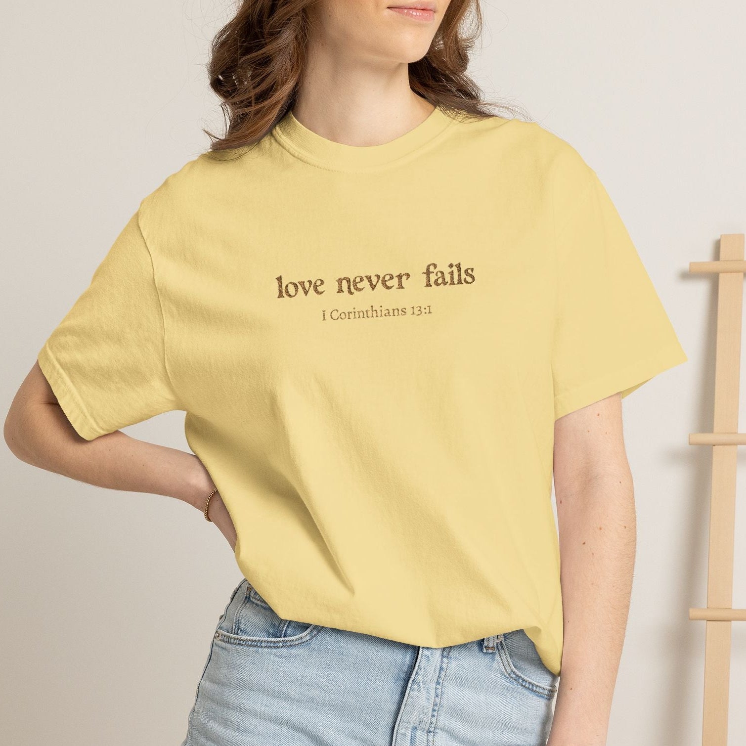 Person wearing a yellow t-shirt with embroidered love never fails logo and denim shorts in a casual setting.