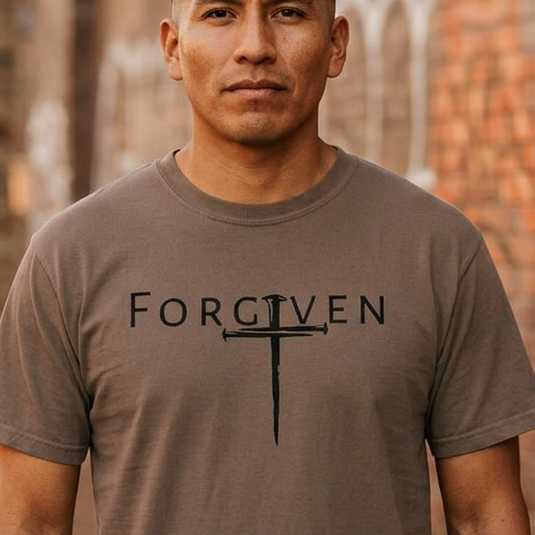 Man wearing a brown t-shirt with 'FORGIVEN' printed on it, standing in front of a graffiti-covered wall.