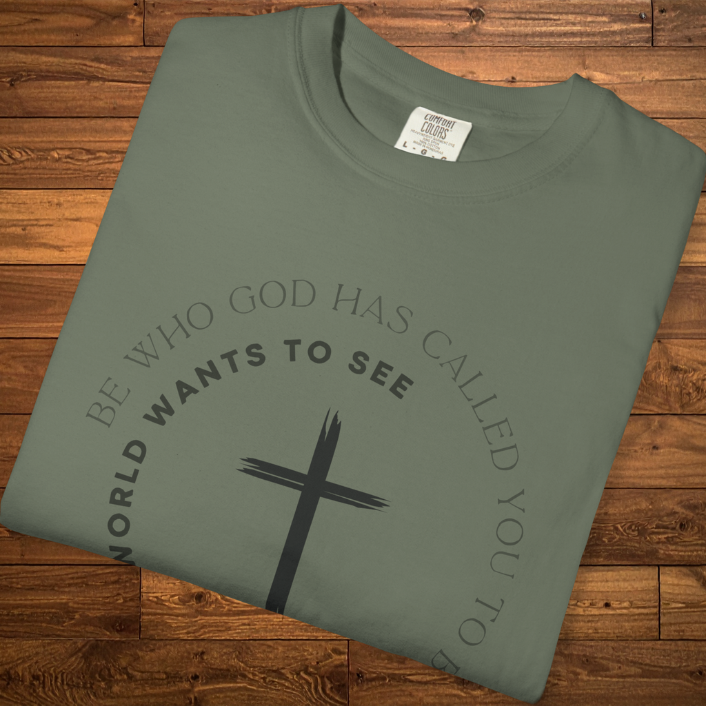 Folded moss green Christian graphic t-shirt featuring a black cross and the message “Be who God has called you to be, not what the world wants to see” in a circular design.
