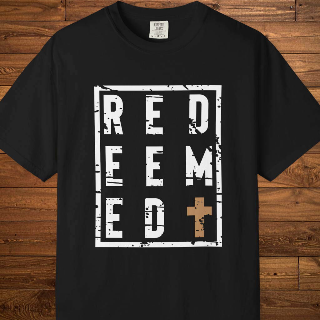 A black short-sleeve t-shirt with a distressed white graphic reading 'RED EEM ED' and a brown cross, displayed flat against a rustic wooden plank background.