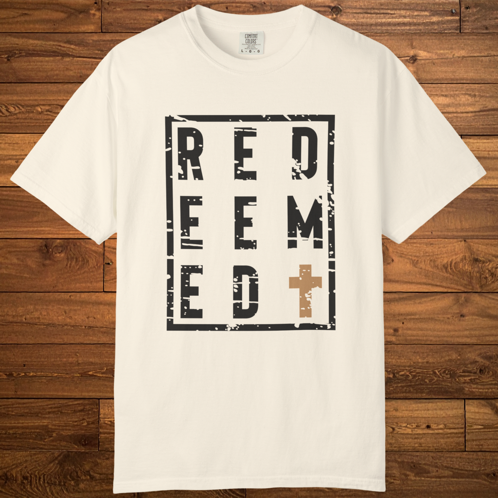 An off-white crewneck t-shirt with a distressed black graphic reading 'REDEEM' and a brown cross, laid flat on a rustic wooden background.